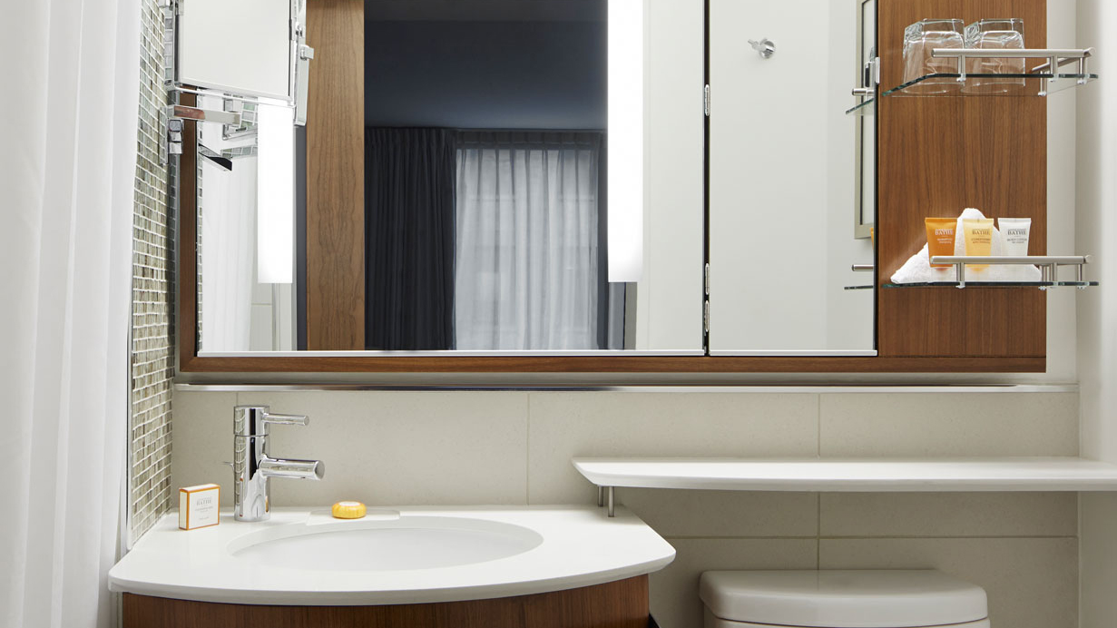 A modern hotel bathroom with a large mirror, a sink, and a toilet.