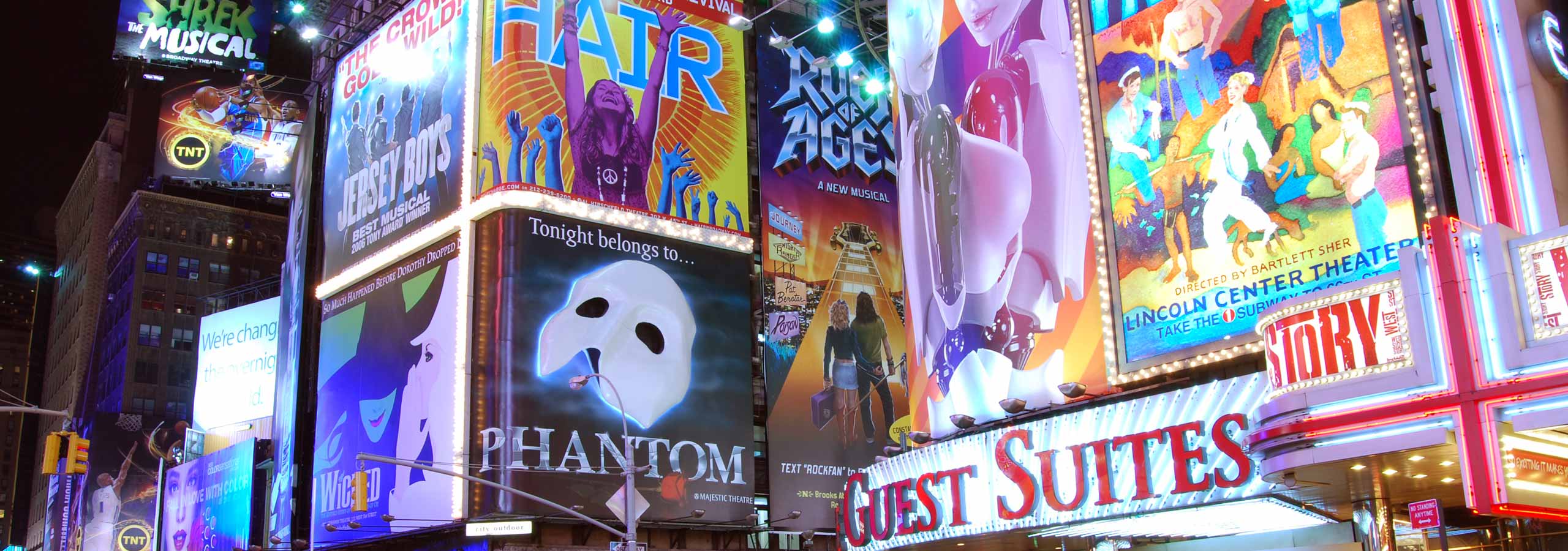 A nighttime view of a vibrant theater district with large digital billboards and advertisements.