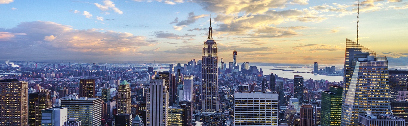 A cityscape at sunset with the Empire State Building in the center