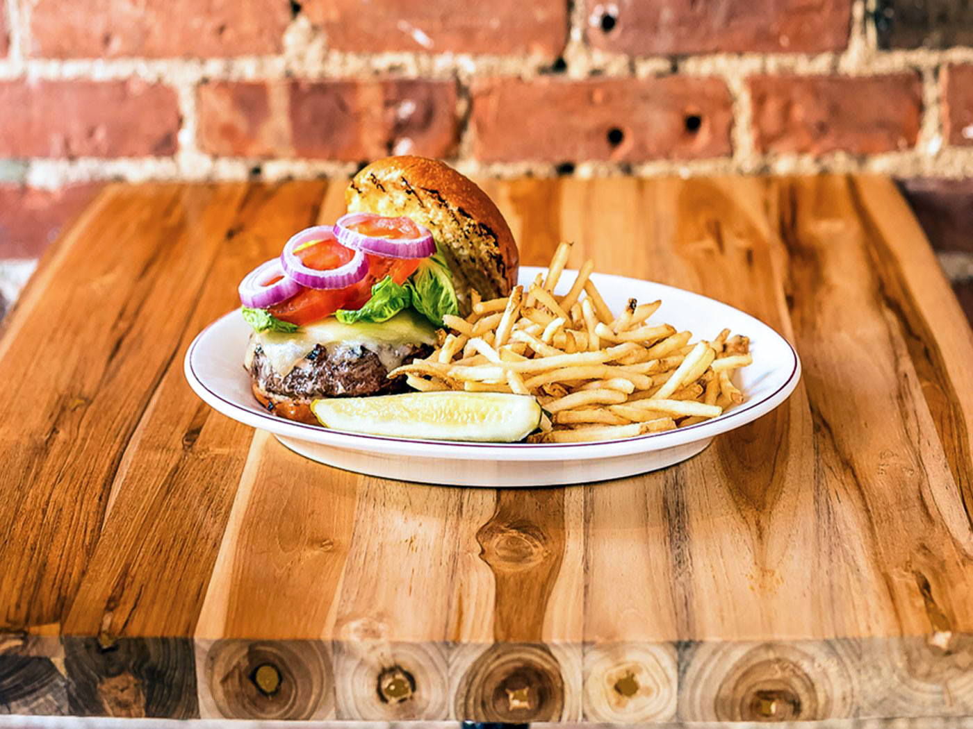 a burger with fries and a pickle on a wooden table