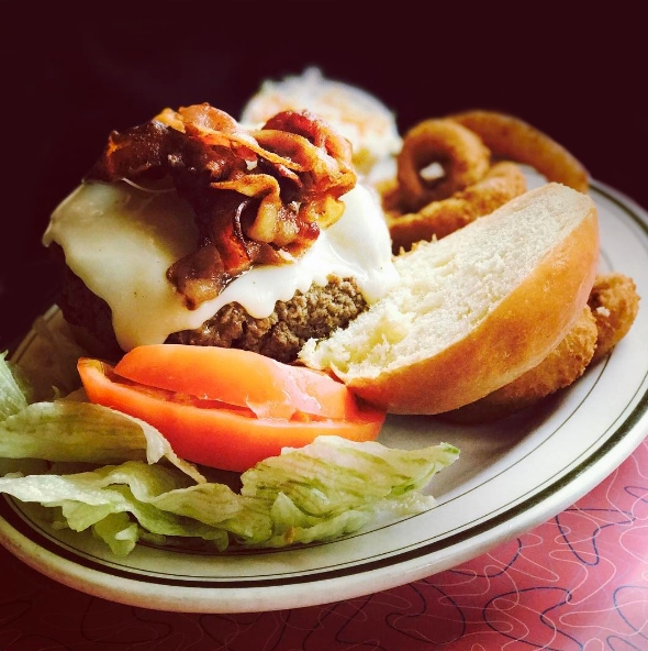 a burger with bacon, cheese, lettuce, tomato, and onion rings on a plate